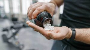 Closeup-of-sporty-muscular-man-arms-showing-sports-and-fitness-supplements-capsules-pills-gym-background.-Healthy-lifestyle-medicine-nutritional-supplements-and-people-concept